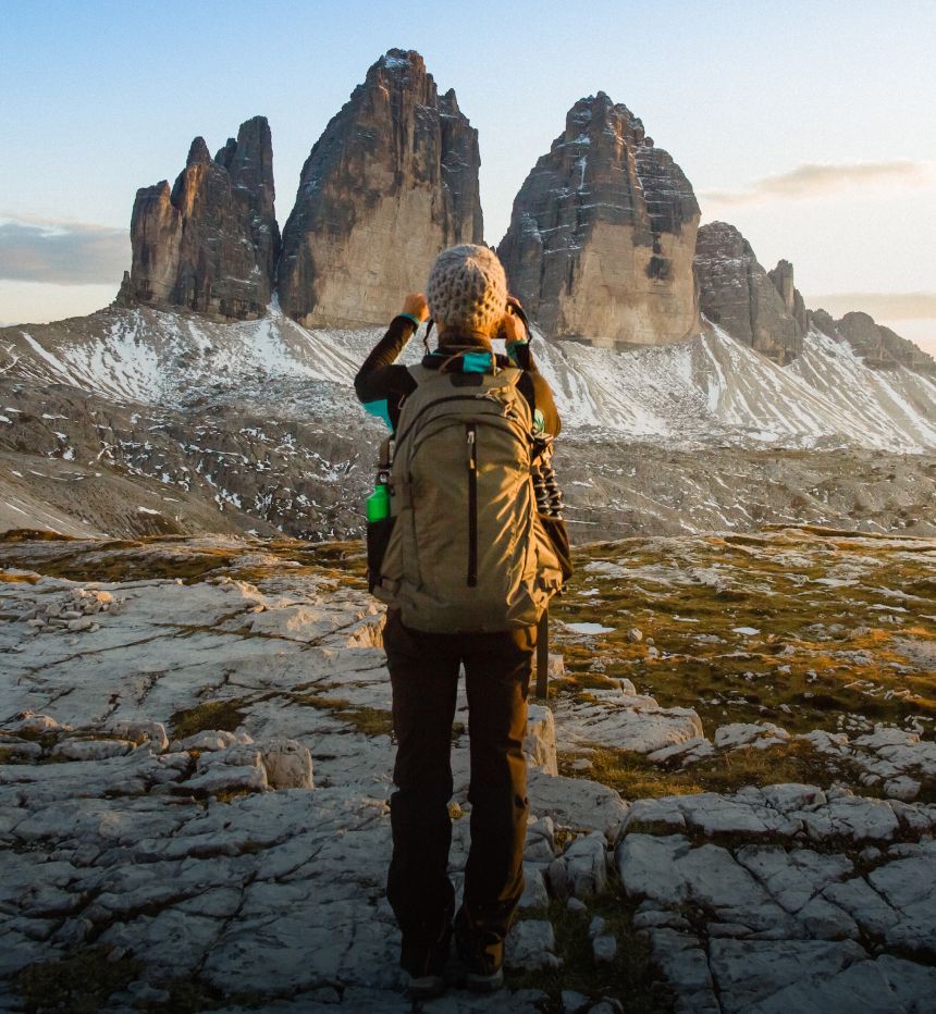 Hiker with large backpack standing on rocks while taking a picture of a rock formation in the distance