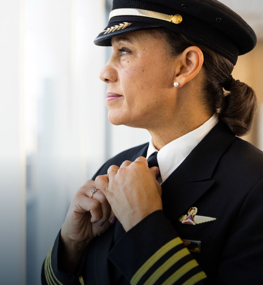 Delta pilot in uniform gazing into the distance and tightening knot on her tie