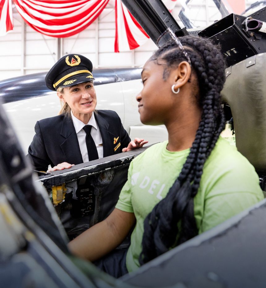 Delta pilot speaking to young girl seated in airplane cockpit