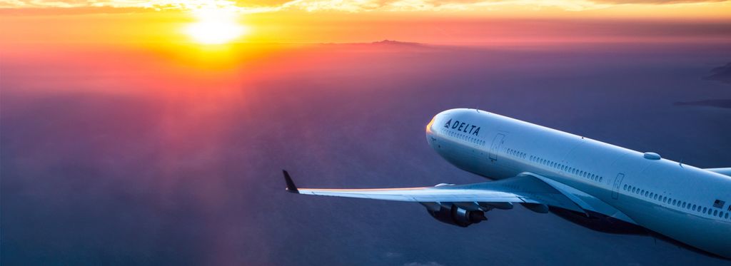 A Delta plane flies towards a deep orange sunset