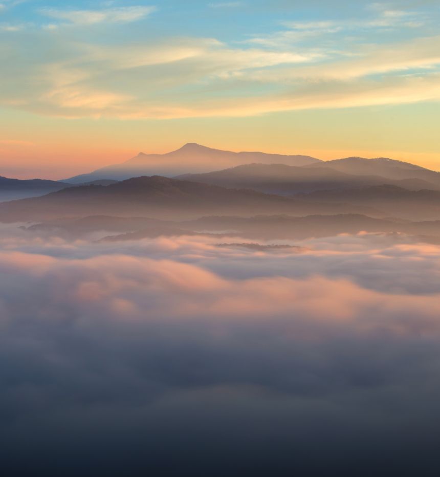 A misty landscape showing layers of mountains in the distance at sunrise