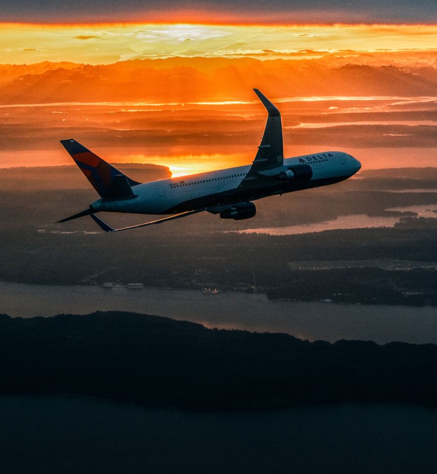 Delta aircraft banking left towards land at sunset