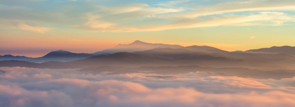 A misty landscape showing layers of mountains in the distance at sunrise