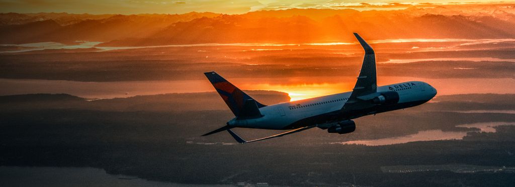 Delta aircraft banking left towards land at sunset