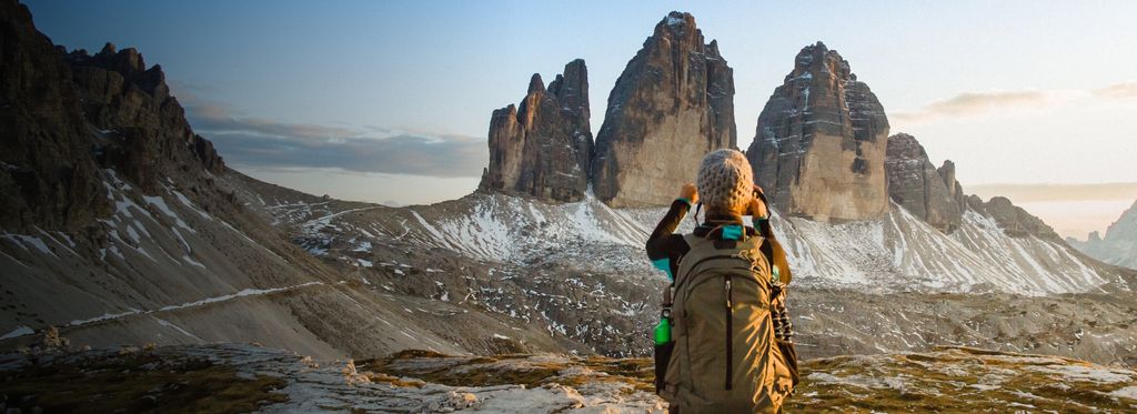 Hiker with large backpack standing on rocks while taking a picture of a rock formation in the distance