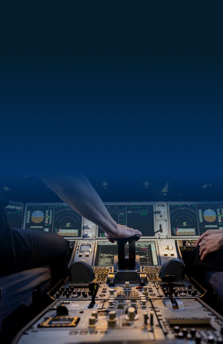 A close up of the controls in the cockpit of an aircraft showing two pilots' hands. One pilot's hand is on the controls, and various instruments, buttons, and screens are visible.