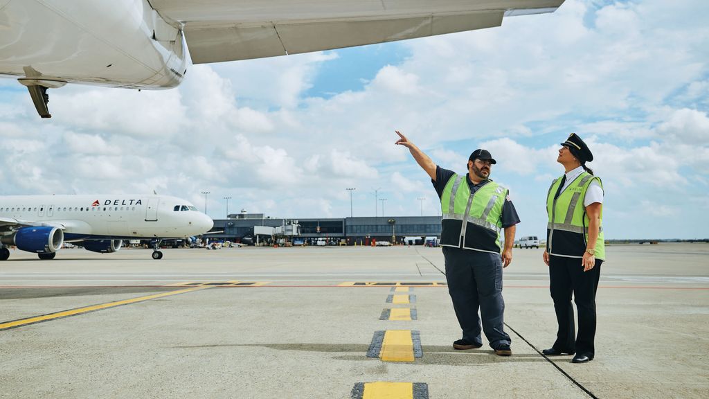 A female pilot and a mechanic, both wearing highvisibility safety vests, inspect an airplane wing on the tarmac.