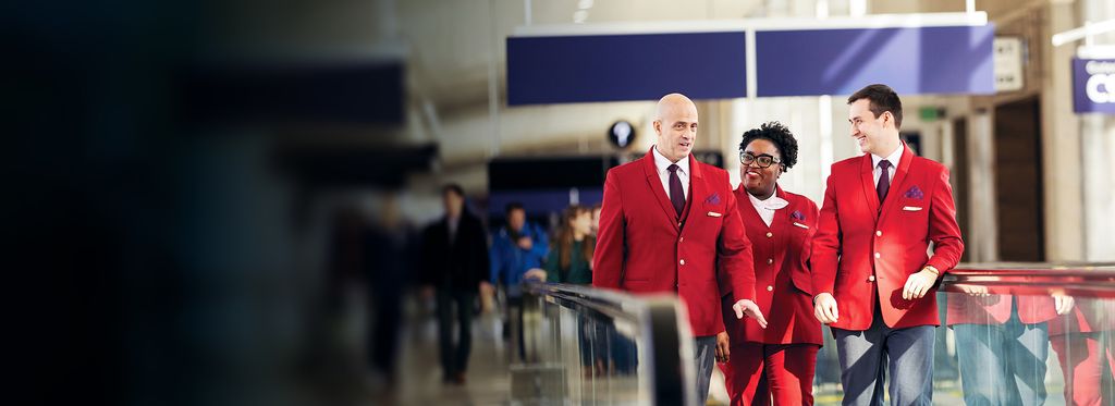Three Delta customer service employees wearing red uniforms, walking on a moving walkway in an airport.