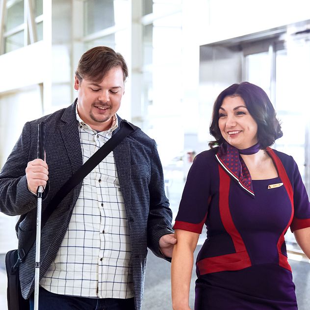 A Delta passenger with a cane is being assisted by a Delta employee in uniform.