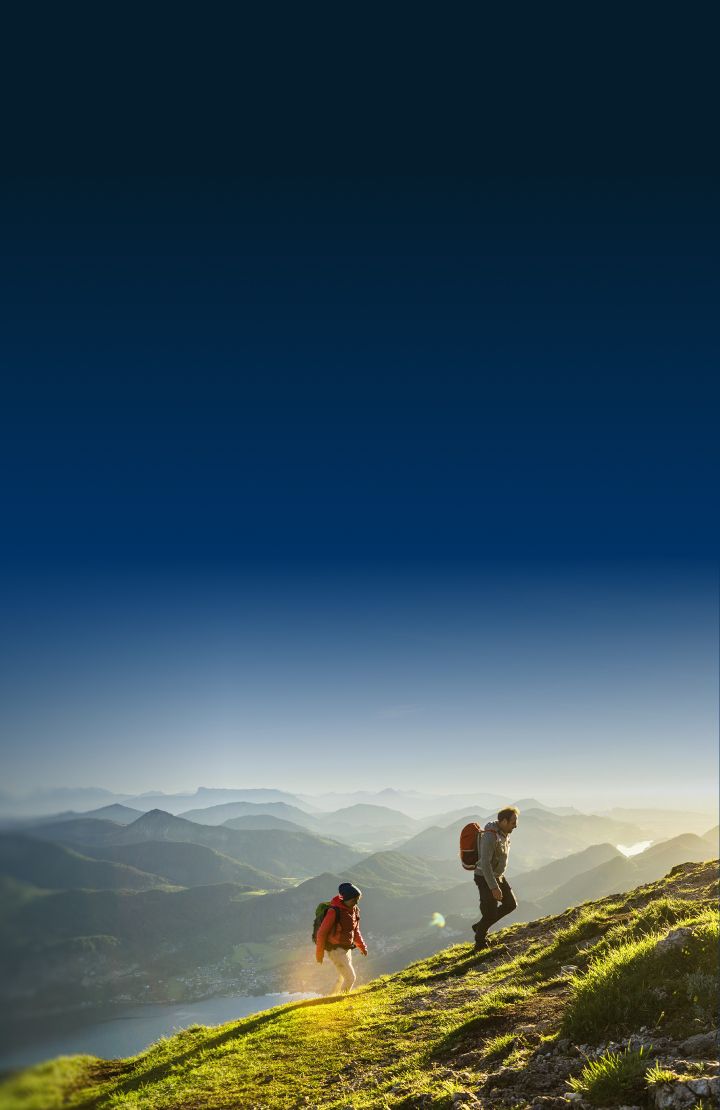Two people hiking up a grassy mountain slope with rocky patches.