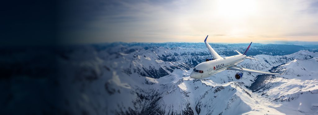 A Delta airplane flying over snowy mountain terrain