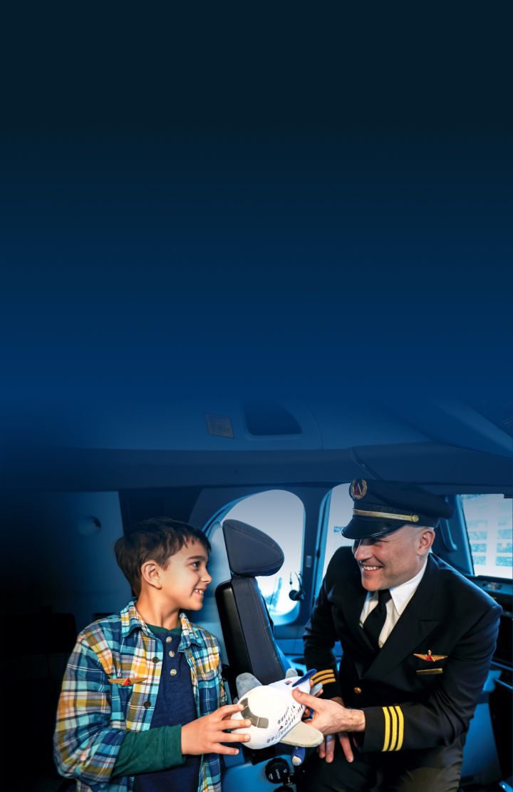 A Delta pilot presenting a toy airplane to a child in the cockpit of an aircraft