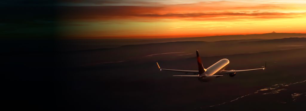 A Delta airplane flies above dark terrain at sunset, with the sky displaying orange and yellow hues.