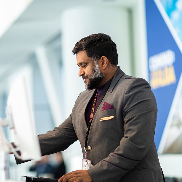 A Delta customer service employee at the airport, standing at a counter with computer monitors.