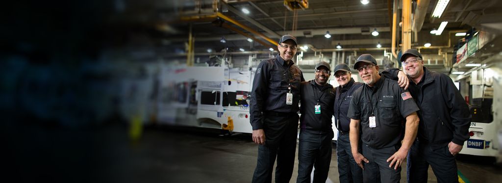 Four Delta mechanics in dark uniforms standing together in an industrial setting.