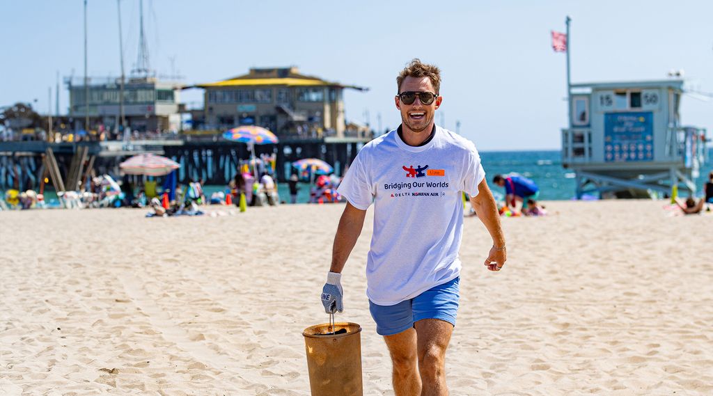 A Delta volunteer is walking on a sandy beach carrying a brown bucket.