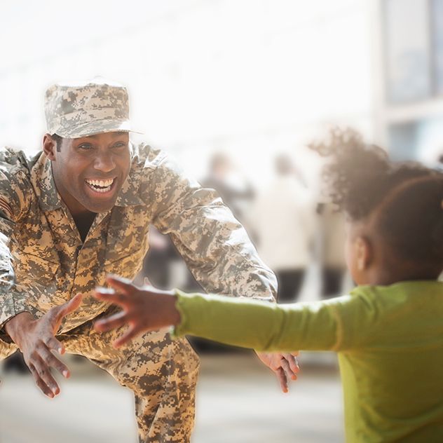 Person in military uniform crouching down with arms extended towards a child who is running towards them with outstretched arms