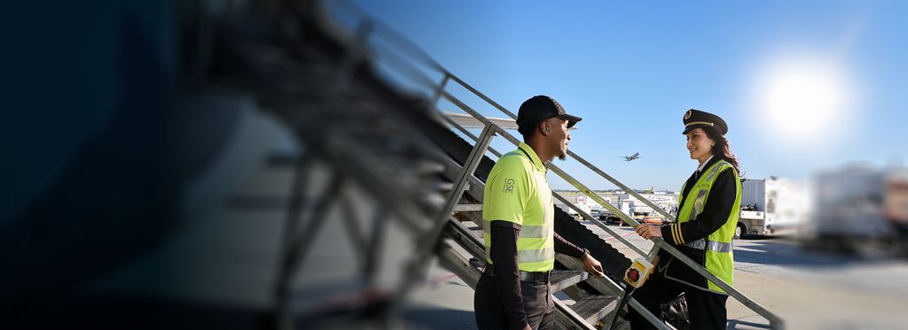 A female Delta pilot and mechanic talk near an aircraft boarding staircase.