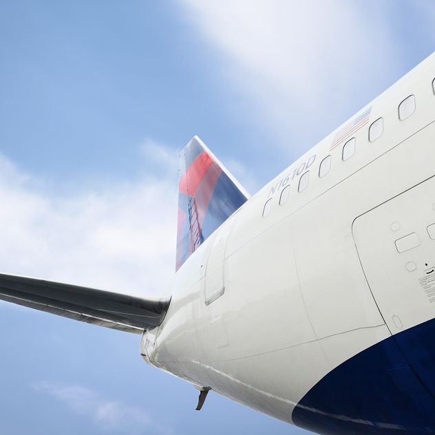 The side view of a Delta airplane's fuselage and tail against a blue sky with some clouds.