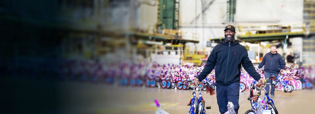 A Delta employee holding two children's bicycles in a large indoor space filled with colorful children's bicycles.