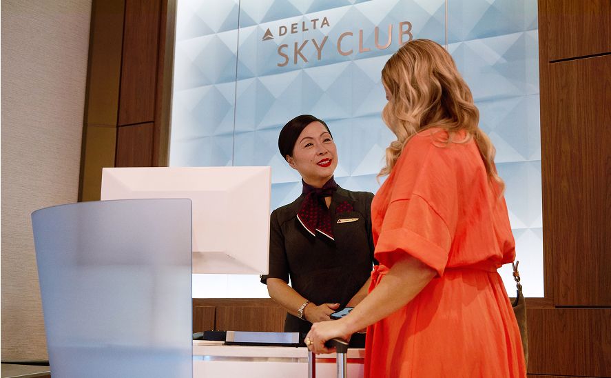 A Delta sky club customer service employee interacting with a customer at a Delta Sky Club reception desk.
