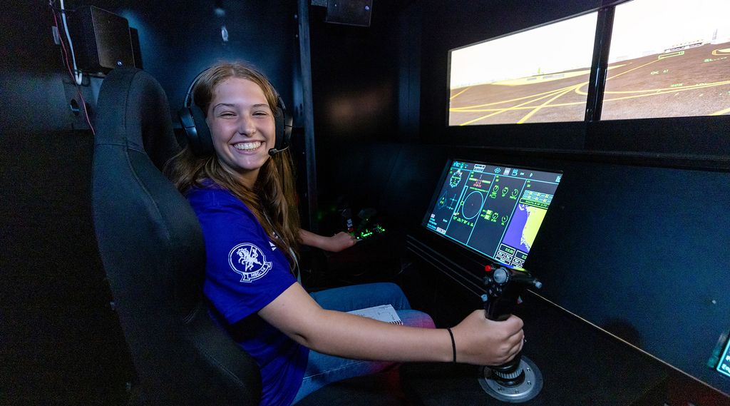 A young person sitting in a flight simulator cockpit, wearing headphones and holding a joystick.
