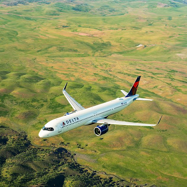 A Delta Air Lines airplane flying over a vast, green landscape