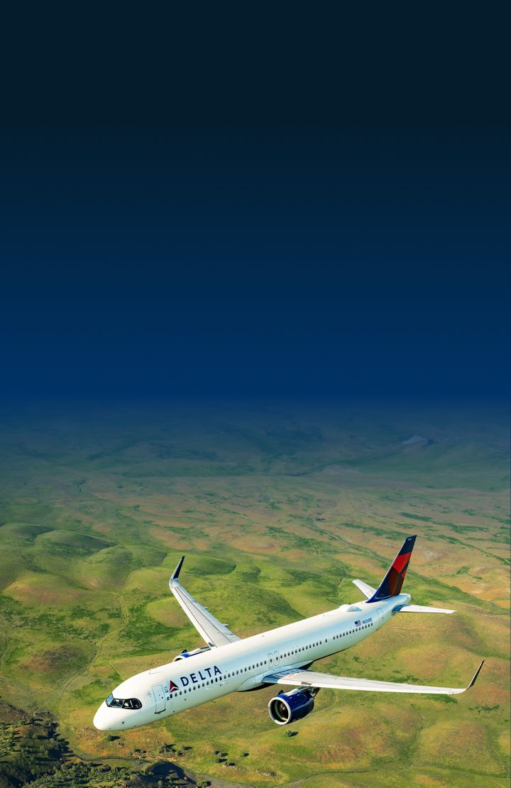 A Delta Air Lines airplane flying over a vast, green landscape