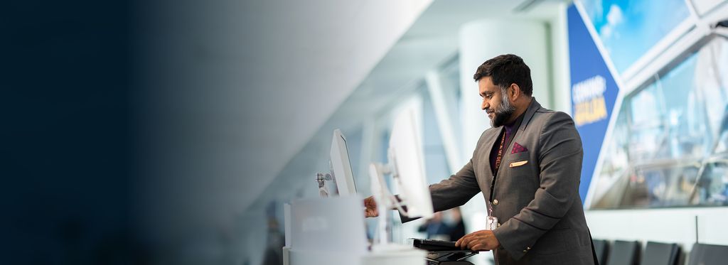 A Delta customer service employee at the airport, standing at a counter with computer monitors.