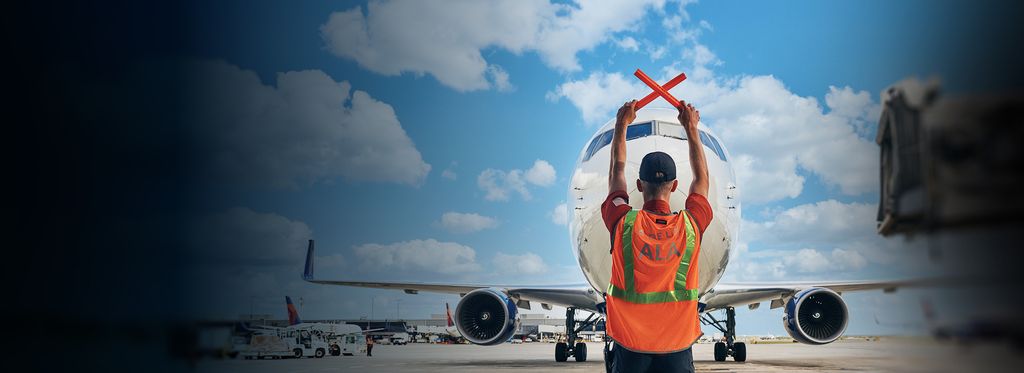 A Delta ground crew member signaling an airplane with red wands.