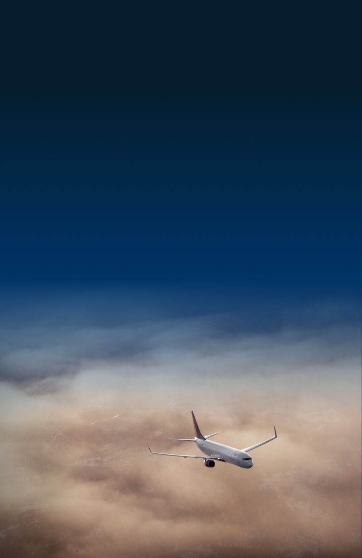 A Delta airplane flying above a mix of light and dark cloud formations.