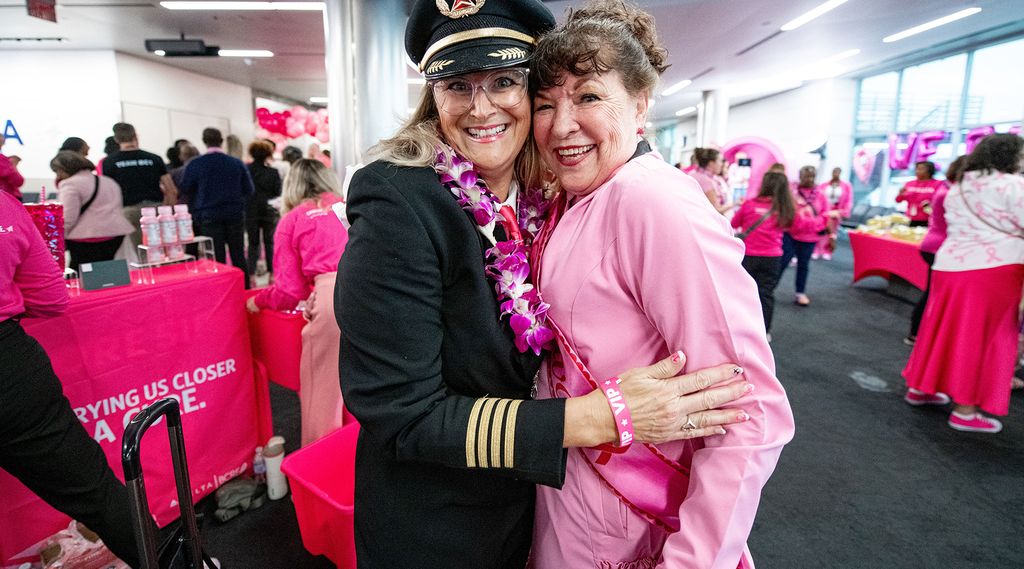 A Delta pilot in uniform and a pink lei hugs a lady dressed in pink at a breast cancer research foundation event.
