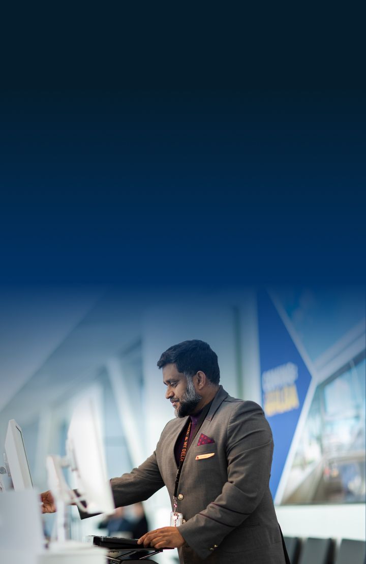 A Delta customer service employee at the airport, standing at a counter with computer monitors.
