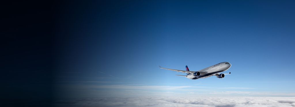 A Delta airplane is flying above a thick layer of clouds with a clear blue sky in the background.
