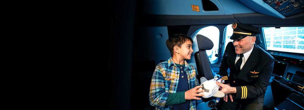 A Delta pilot presenting a toy airplane to a child in the cockpit of an aircraft