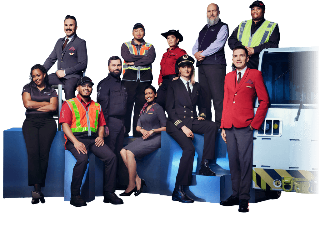 A group of Delta employees in various uniforms in front of an airplane tail with the Delta logo.