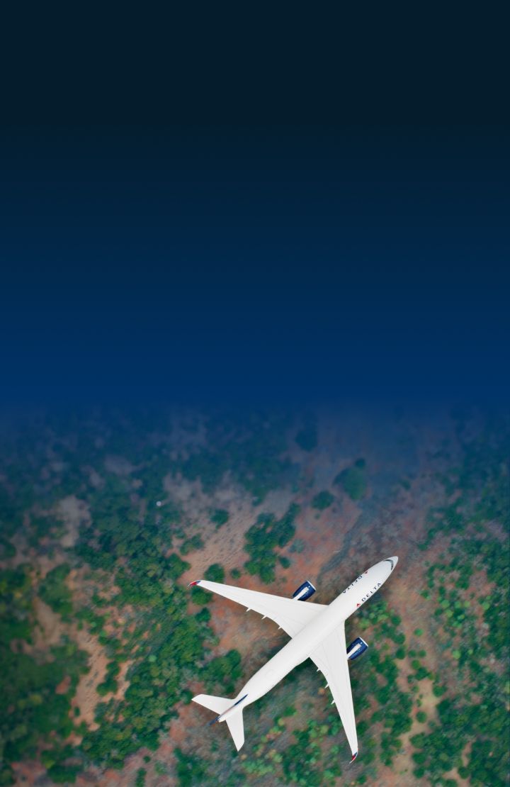 Aerial view of a Delta airplane flying over a landscape with patches of green vegetation and brown soil.