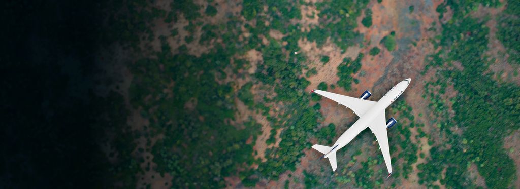 Aerial view of a Delta airplane flying over a landscape with patches of green vegetation and brown soil.