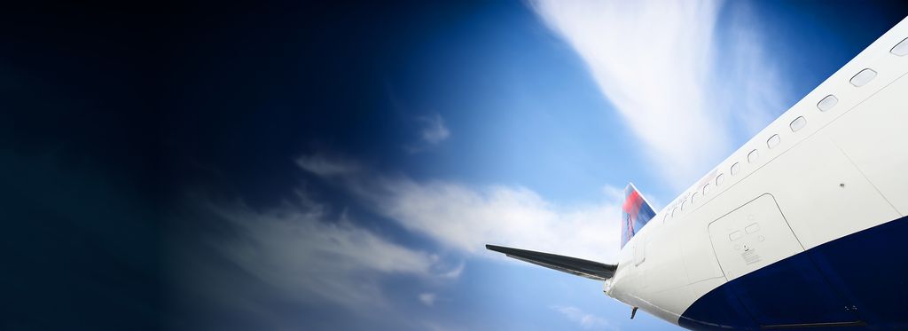 The side view of a Delta airplane's fuselage and tail against a blue sky with some clouds.