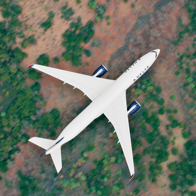 Aerial view of a Delta airplane flying over a landscape with patches of green vegetation and brown soil.