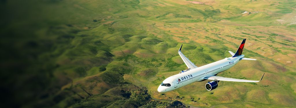 A Delta Air Lines airplane flying over a vast, green landscape