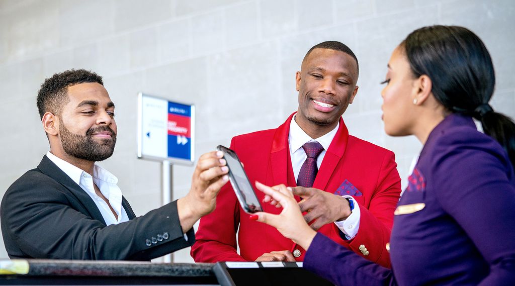 Two Delta employees assist a customer at an airport check-in counter.