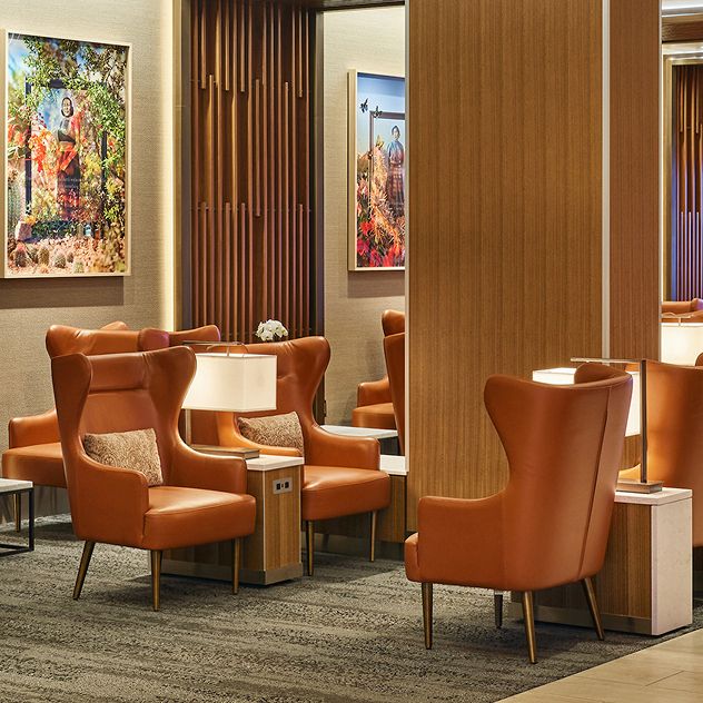 A Delta Sky Club lounge with warm lighting, leather armchairs, wood paneling, and elegant decor, including artwork and a statement chandelier.