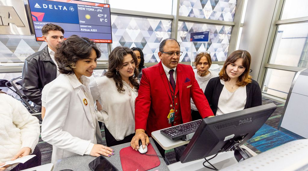 A group of young people standing behind an airport check-in counter during a job shadow with a Delta Air Lines agent.