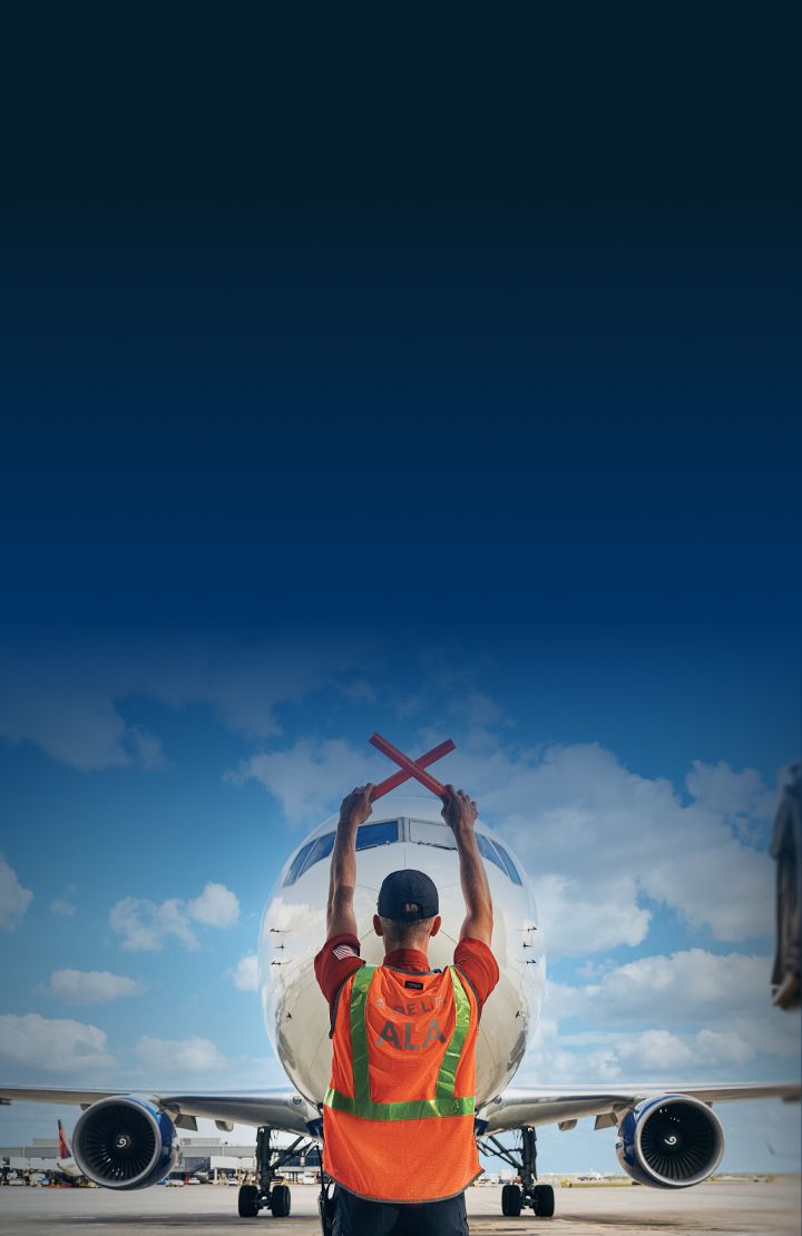 A Delta ground crew member signaling an airplane with red wands.