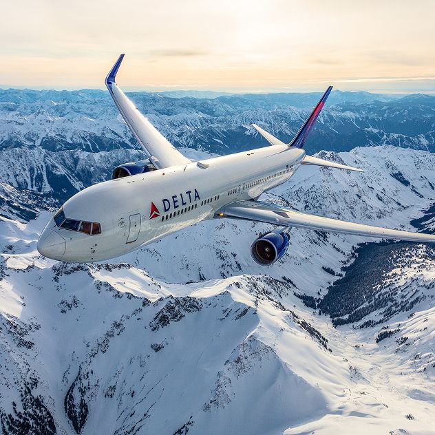 A Delta airplane flying over snowy mountain terrain