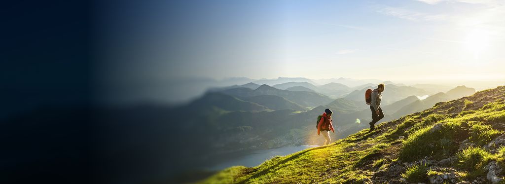 Two people hiking up a grassy mountain slope with rocky patches.
