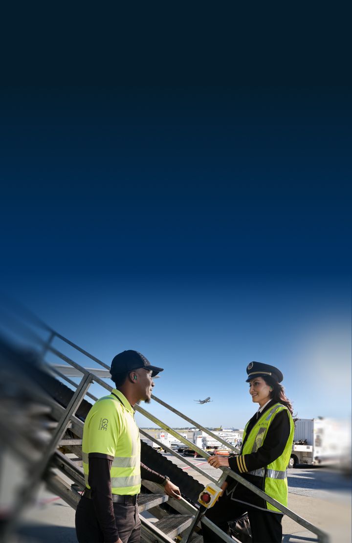 A female Delta pilot and mechanic talk near an aircraft boarding staircase.
