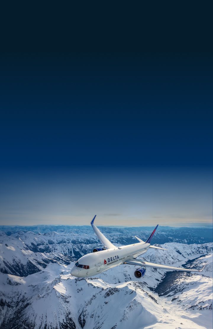 A Delta airplane flying over snowy mountain terrain