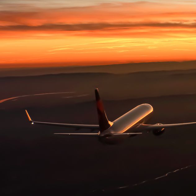 A Delta airplane flies above dark terrain at sunset, with the sky displaying orange and yellow hues.
